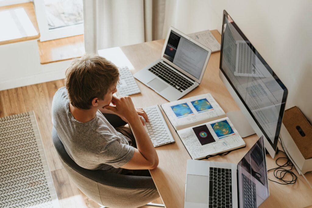 pexels-photo-4974922-4974922 Top view of young programmer working on multiple laptops in a modern office setting.